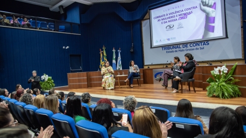 TCE-MS ouve gestoras municipais e propõe ação conjunta para fortalecer políticas públicas às mulheres A conference on combating violence against women and girls, featuring speakers on stage and an audience engaged in discussion.