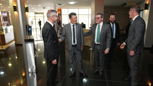A group of five men in business suits are engaged in conversation and shaking hands in a modern office lobby.