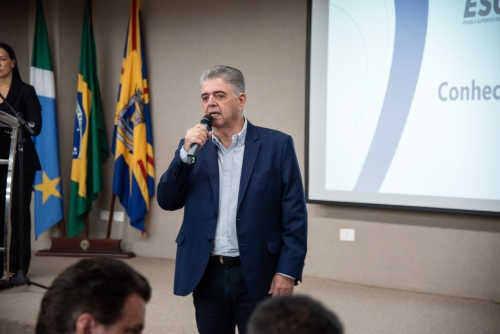 Comitiva de estudantes e servidores de Chapadão do Sul conhecem o TCE-MS A man in a suit speaks into a microphone at an event, with flags in the background.
