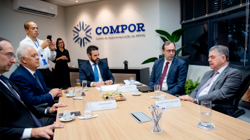 A group of professionals is seated around a conference table in a modern office, discussing matters related to the organization "COMPOR."