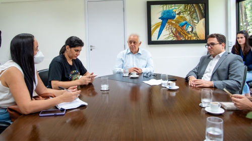 A meeting at a table with four people discussing, surrounded by a bright room and a colorful parrot painting on the wall.