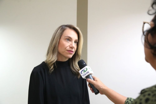 A woman with long, blonde hair is speaking during an interview, while another person holds a microphone.