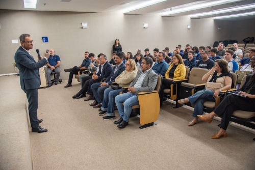 Comitiva de estudantes e servidores de Chapadão do Sul conhecem o TCE-MS A speaker addresses an audience in a conference room, with attendees seated in rows, engaged and attentive.